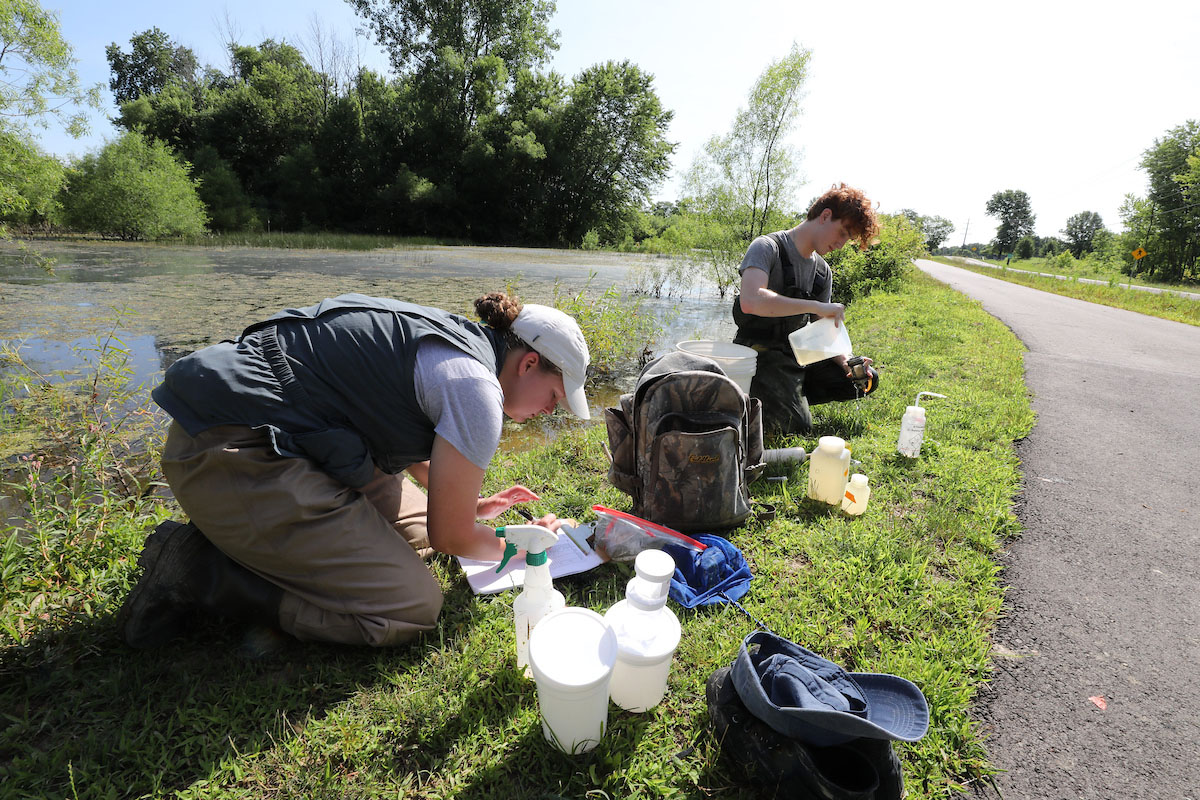 Two Miami graduate students next to a pond measuring samples of the water