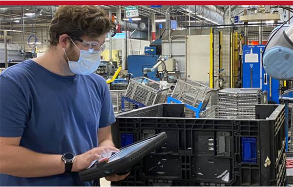 A student with face mask writes on an ipad in a factory warehouse workplace