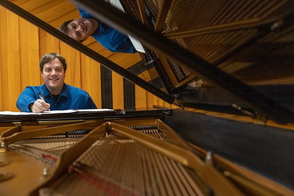 Martin Hebel sitting at piano with pen in hand for composing music