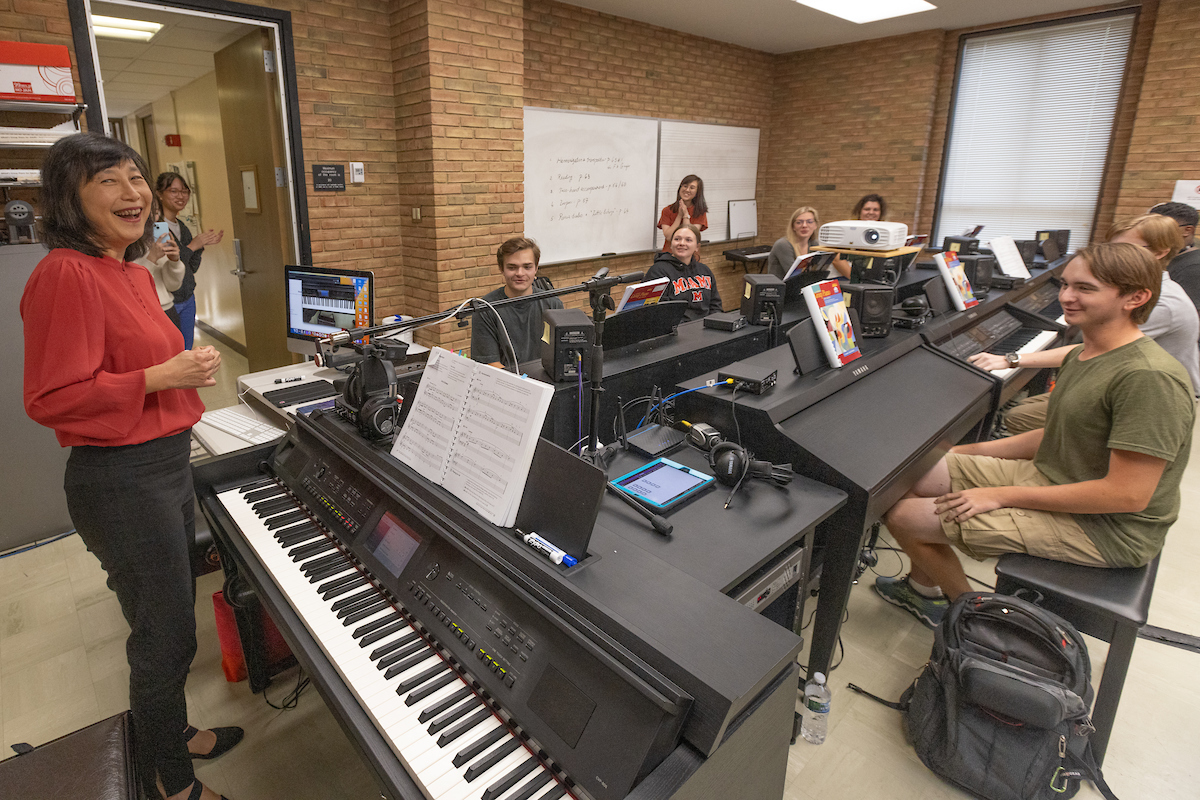 A professor teaches a class in a piano lab.