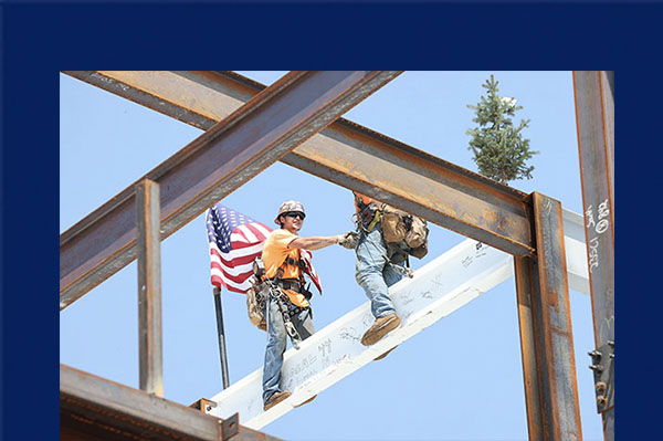 top out ceremony 2 men shake hands on the top beam of the data science building , with a flag and fir tree