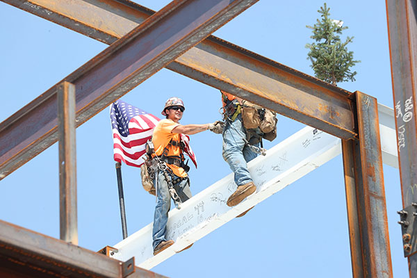 top out ceremony 2 men shake hands on the top beam of the data science building , with a flag and fir tree