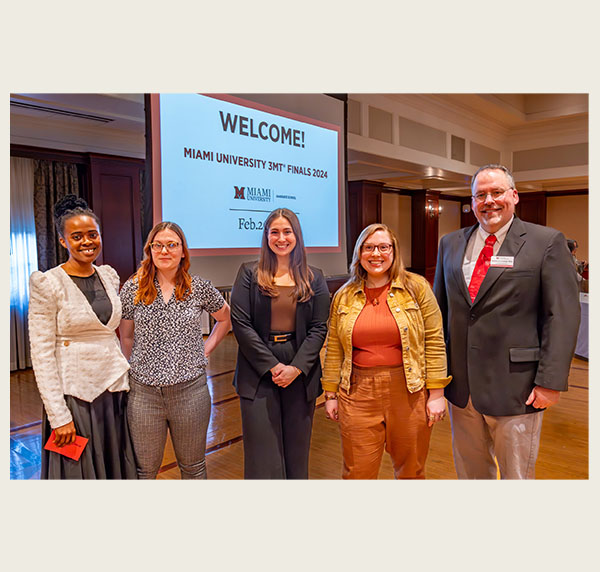 Four graduate students and Michael Crowder stand in front of a Welcome to 3MT slide in the Heritage Room 