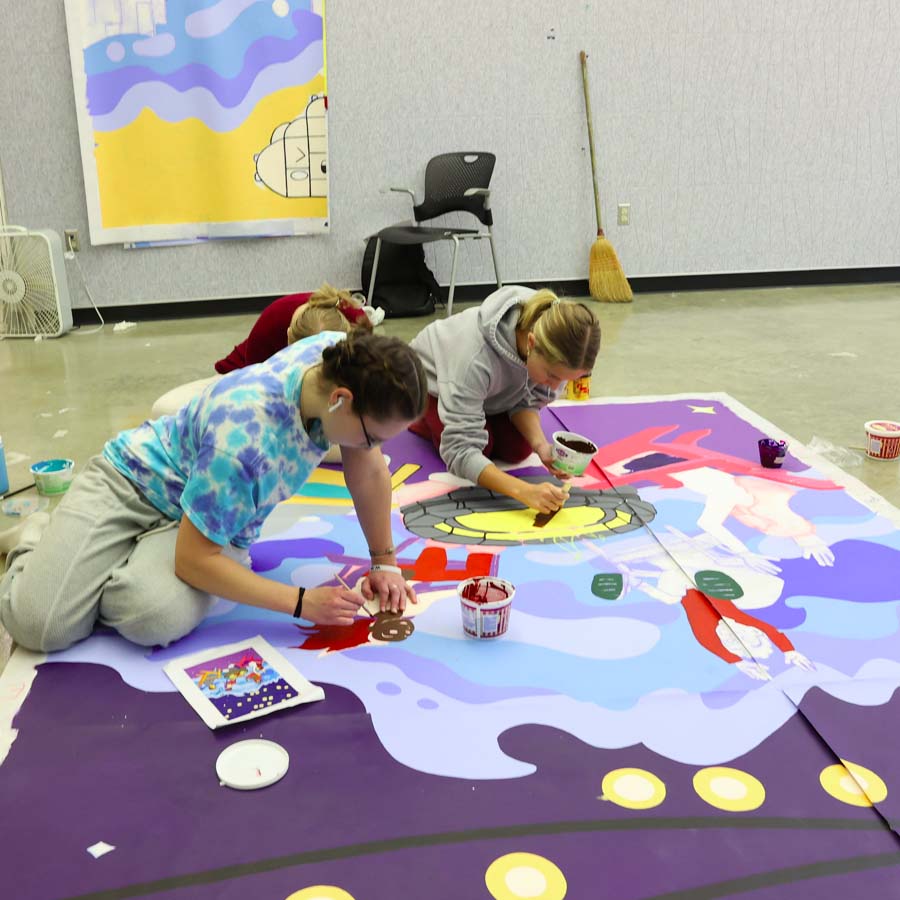 3 students paint a mural on polytab spread out on the floor