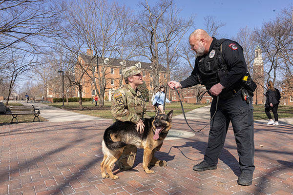 mupd officer Keith Hibbard and K-9 Leo greet a student at the seal. The ROTC student has an arm around Leo the german sheperd