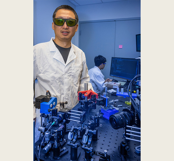 Hui Wang stands in his lab wearing protective eyewear.