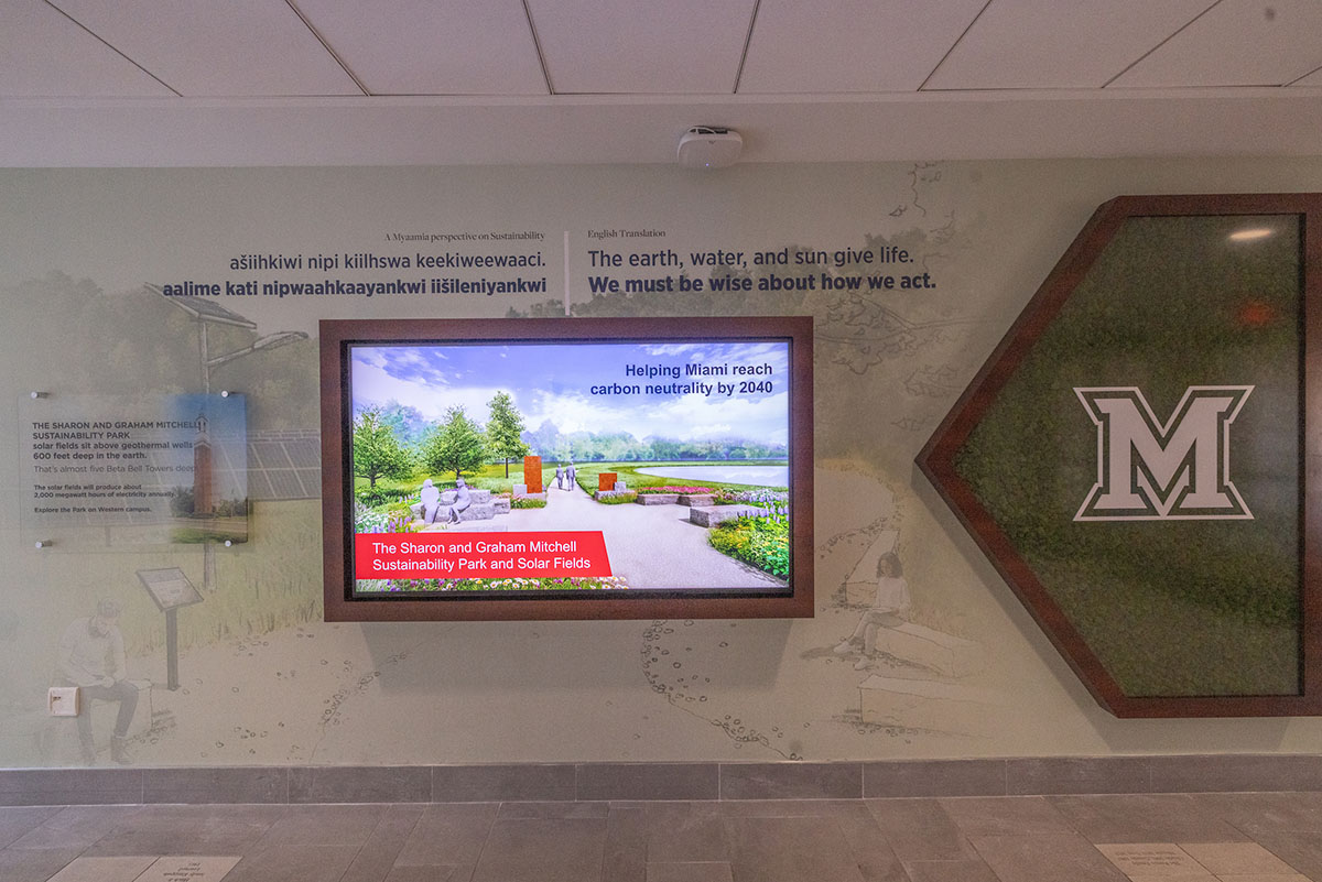 sustainability wall in armstrong student center with large graphic of park, a large digital monitor displaying a slide with miami's solar fields, and a large beveled M on a background of preserved moss