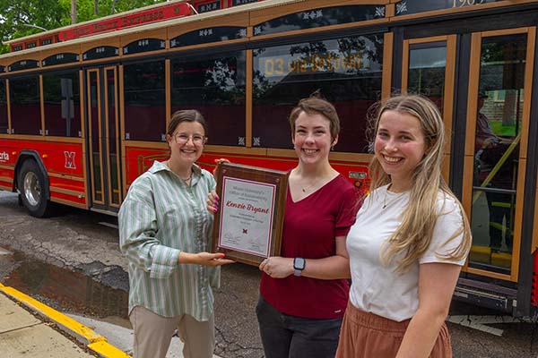 Olivia Herron, Kenzie Bryant, and Alex Miller pose in front of the BCRTA Miami Trolley Bus. Kenzie holds a plaque with Sustainability Champion  Kenzie Bryant