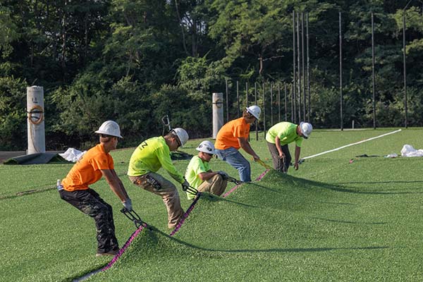 Several workers pull on large hooks grabbing the synthetic turf at Chestnut Fields to pull it smooth